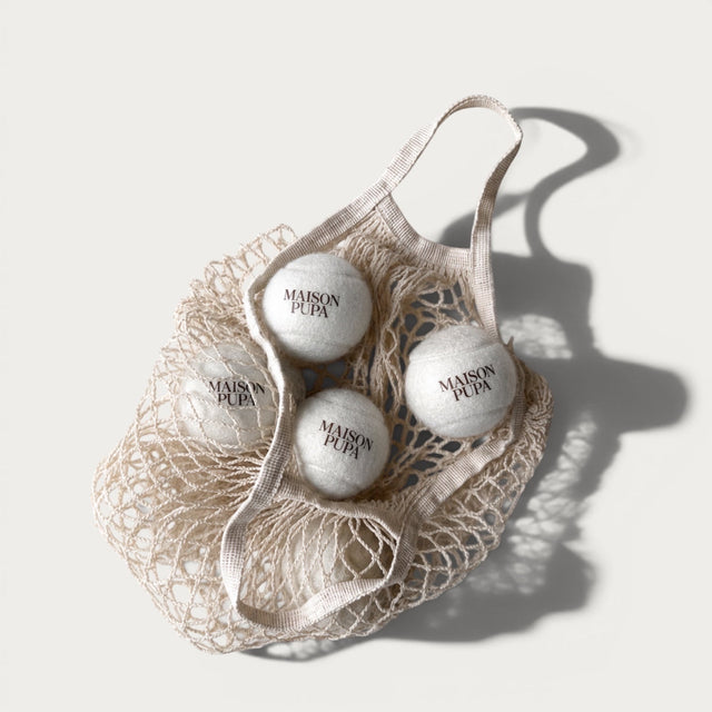 Maison Pupa tennis set featuring three cream felt tennis balls with wine-colored branding inside a cotton mesh bag.